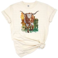 A longhorn cow standing in a desert landscape with cacti and rustic western elements.