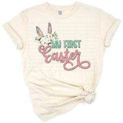A cute baby pink floral bunny ears design with 'My First Easter' script and soft pastel accents.